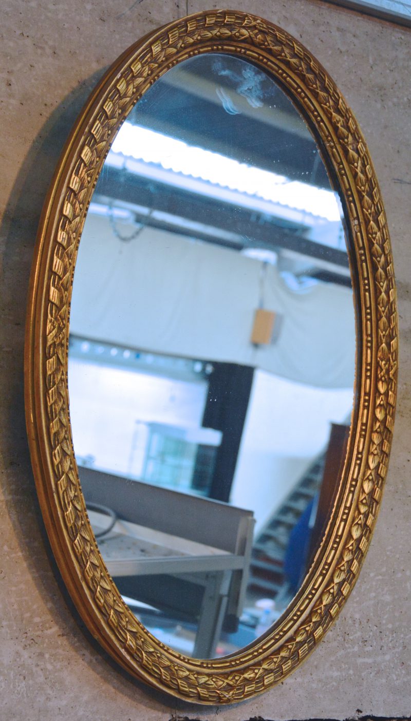 Een ovale spiegel in verguld houten lijst.