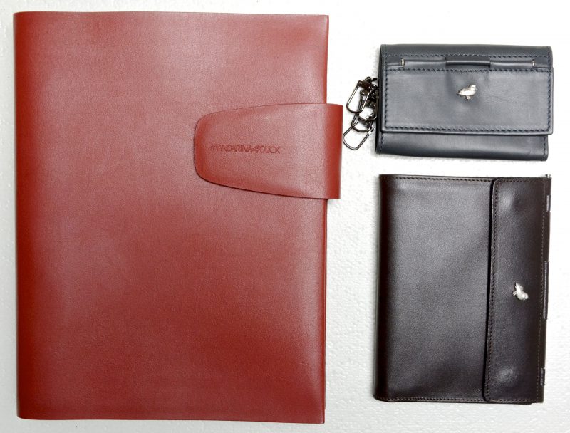 Een contactboek-planner in rood lederen kaft, een herenportefeuille van zwart leder en een sleutelhanger van grijs leder.