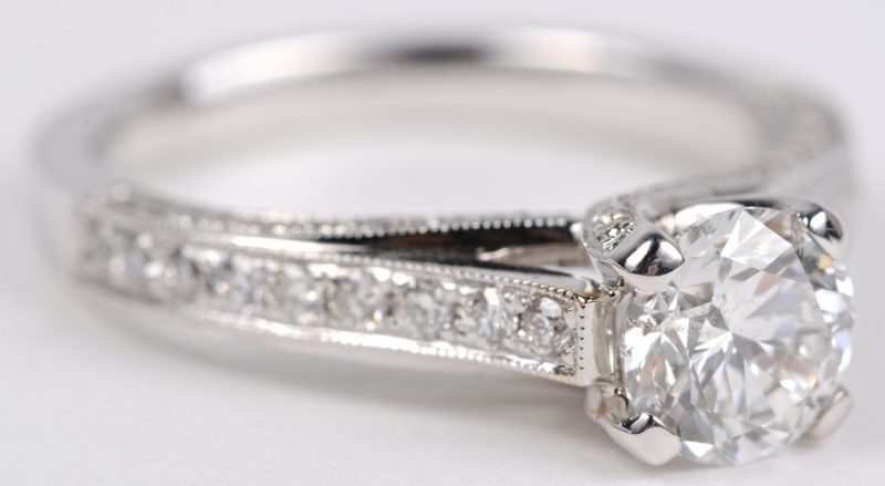 Een 18 karaats wit gouden ring bezet met een centrale diamant van ± 1,02 ct. H. SI1 en diamanten met een gezamenlijk gewicht ± 0,44 ct.