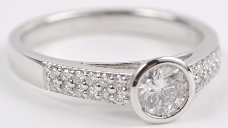 Een 18 karaats wit gouden ring bezet met een centrale diamant van ± 0,40 ct. en diamanten met een gezamenlijk gewicht ± 0,19 ct.