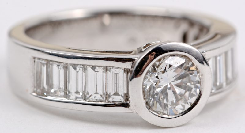Een 18 karaats wit gouden ring bezet met een centrale diamant van ± 0,70 ct. en diamanten met een gezamenlijk gewicht ± 0,88 ct.