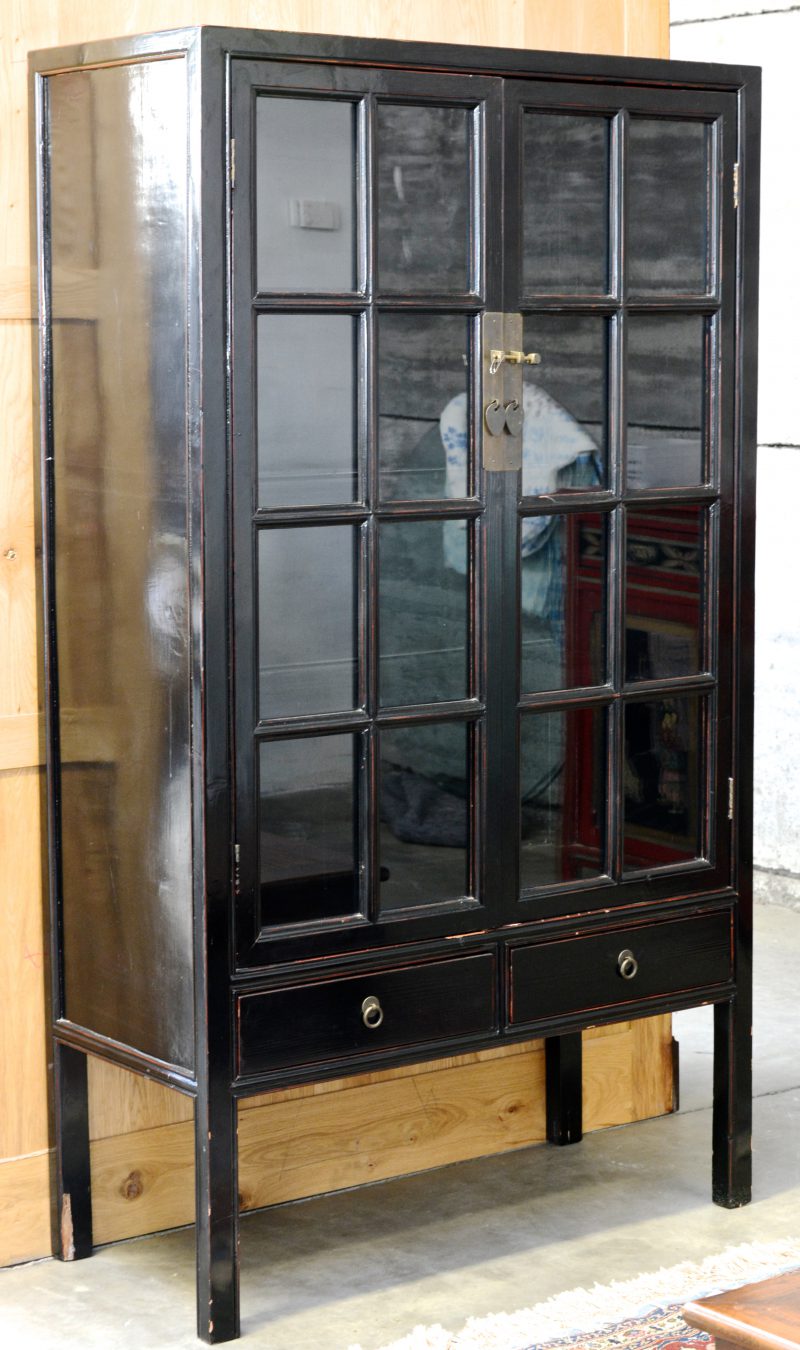 Een Chinese vitrinekast van zwartgelakt hout met twee deuren en twee laden.