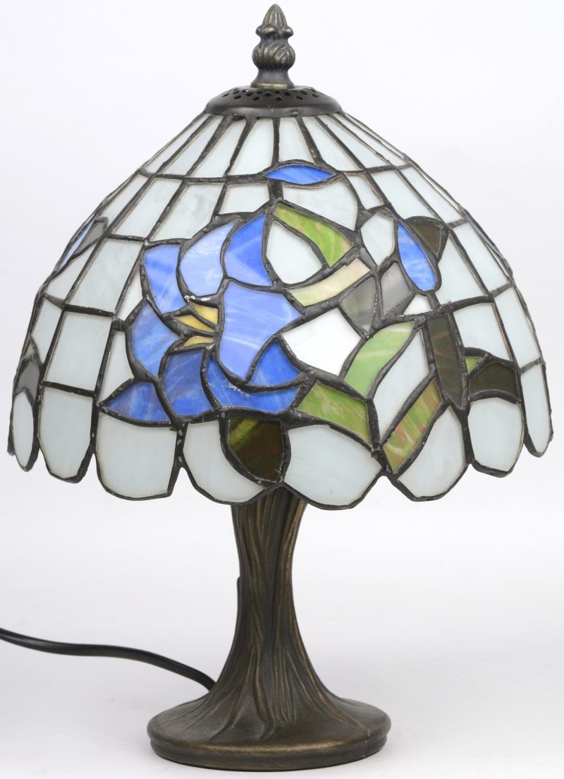 Een bronzen lampvoet met een kap van glas in lood, versierd met een bloemendecor.