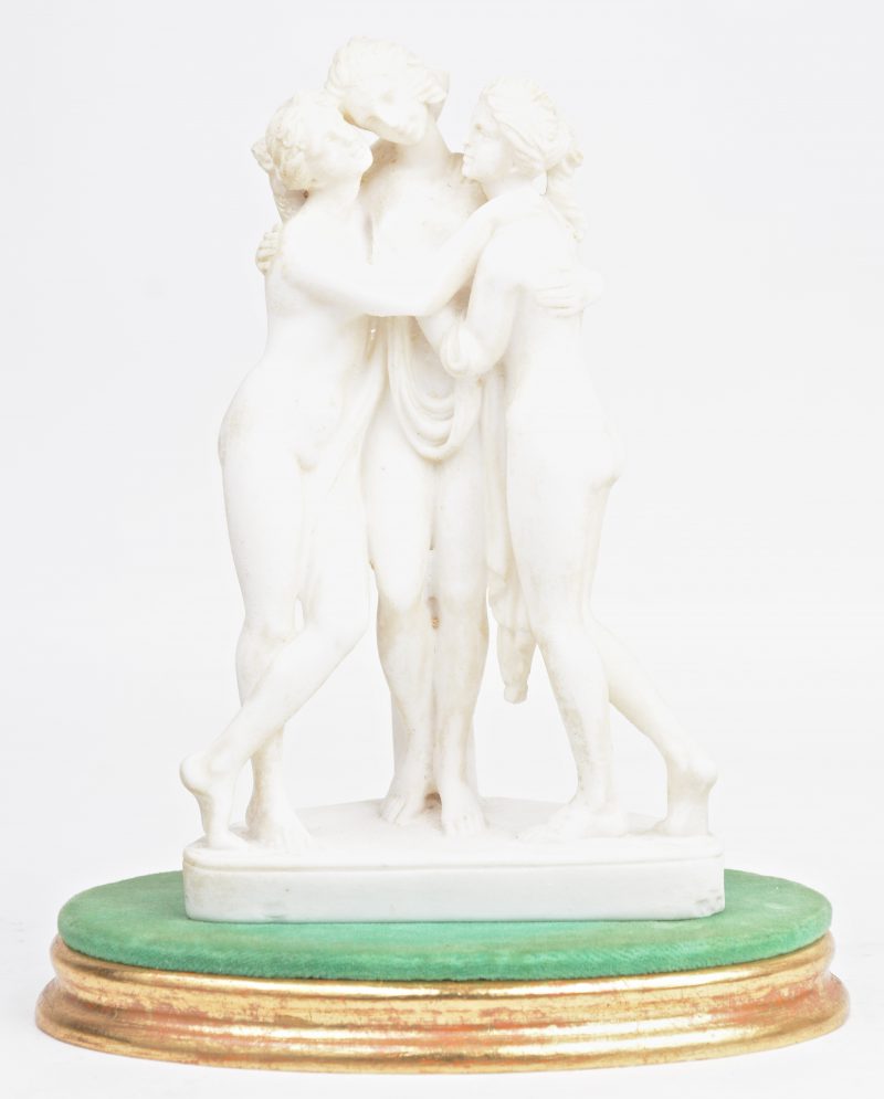 “De drie gratiën”. Een beeldje van wit composiet op houten voetstuk.