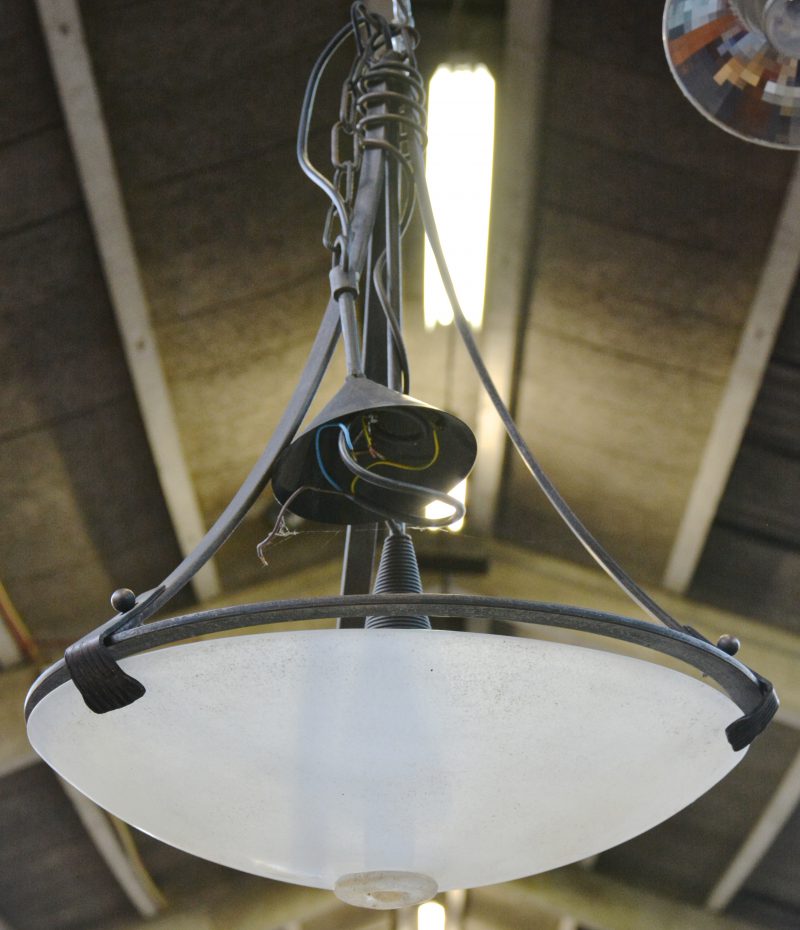 Een hanglamp van smeedijzer met een glazen kap.
