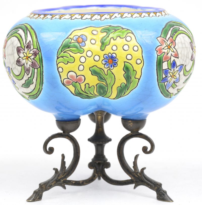 Een potje van  meerkleurig aardewerk, versierd met een meerkleurig reliëfdecor van bloemen en op een metalen driepoot. Vermoedelijk Longwy.