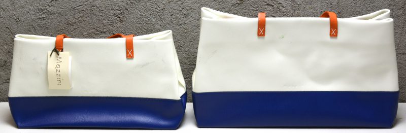 Twee handtassen van blauw, wit en oranje leder, waarbij één in stofhoes. Slijtage aan de draagriempjes.