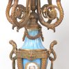 Driedelig klokstel van verguld metaal en versierd met diverse plaquettes van Parijs’ porselein met romantische voorstellingen op lichtblauwe fond. Pendule en twee kandelaars. XIXde eeuw.