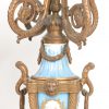 Driedelig klokstel van verguld metaal en versierd met diverse plaquettes van Parijs’ porselein met romantische voorstellingen op lichtblauwe fond. Pendule en twee kandelaars. XIXde eeuw.