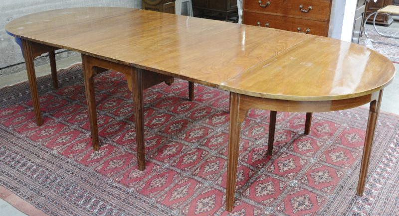 Een Engelse tafel van mahoniehoutfineer, bestaande uit een centraal deel met klapbladen en twee losse halfronde uiteinden. Met twee extra verlengbladen.