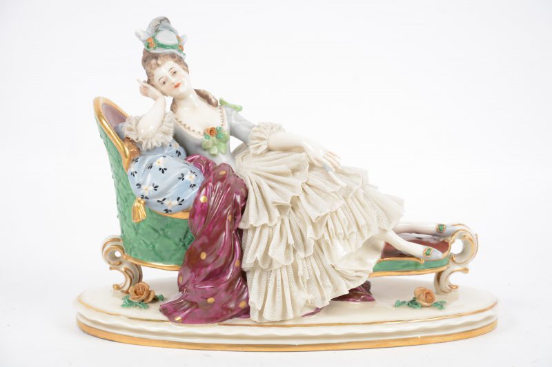 Een liggende dame in XVIIIe eeuwse klederdracht van meerkleurig en verguld porselein. Kleine schade aan de jurk.