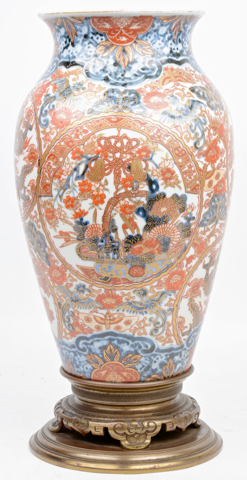 Een porseleinen vaas van Imari porselein met een decor van draken en vegetatie. Japan, XIXde eeuw. Op een koperen voetstuk.