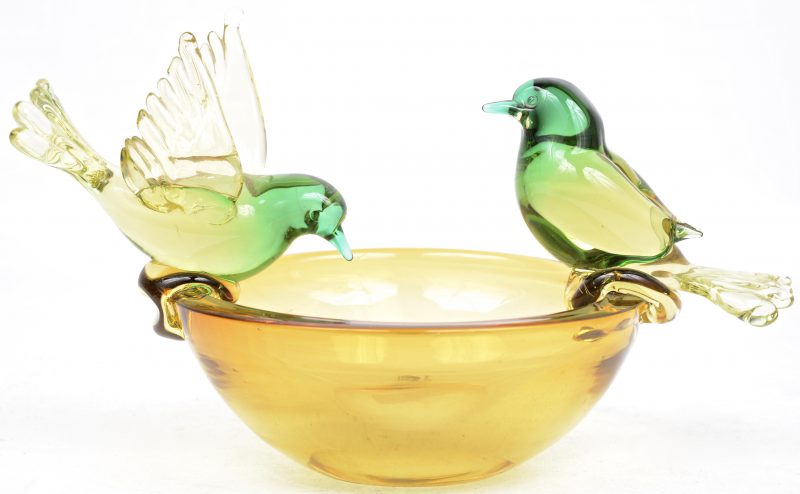Een kommetje van amberkleurig glas met twee groene vogeltjes op de rand.