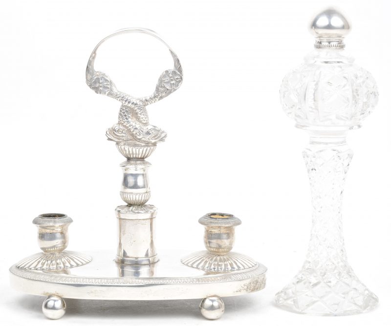 Een dubbele kandelaar met handvat in de vorm van barokke dolfijnen van zilver en parfumflesje van geslepen kleurloos kristal met een zilveren dopje. Beide met Belgische importkeur. XIXe eeuw.