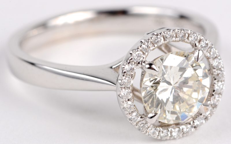 Een 18 karaats wit gouden ring bezet met een centrale diamant van ± 1,17 ct. J. SI1 en diamanten met een gezamenlijk gewicht ± 0,44 ct.
