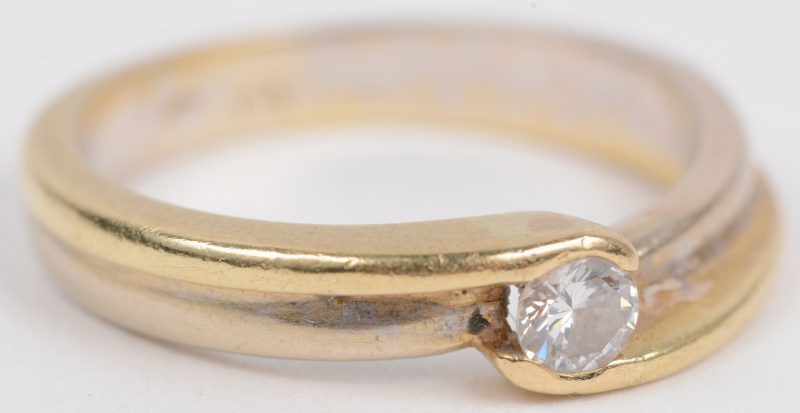 Een 18 karaats wit en geel gouden ring bezet met één briljant van ± 0,15 ct.