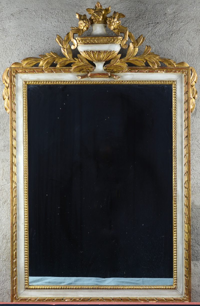 Een gebeeldhouwde spiegel, bovenaan versierd met een siervaas met bloemen en lauriertakken.