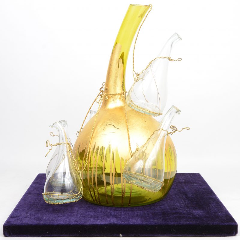 Een glazen tulpenvaas, opgebouwd uit een grote, met goudverf beschilderde groene vaas en zes kleinere kleurloze exemplaartjes.