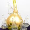 Een glazen tulpenvaas, opgebouwd uit een grote, met goudverf beschilderde groene vaas en zes kleinere kleurloze exemplaartjes.