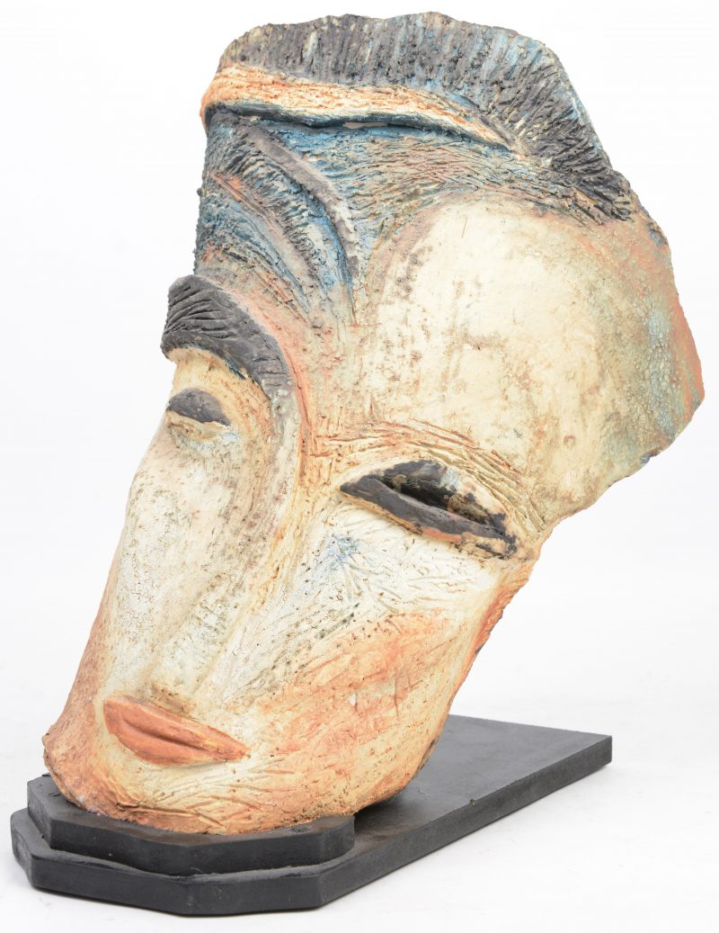 Een Italiaans masker van gepolychromeerd aardewerk op houten sokkel.