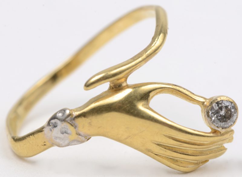 Een 18 karaats wit en geel gouden ring in de vorm van een hand bezet met een briljant van ± 0,10 ct.