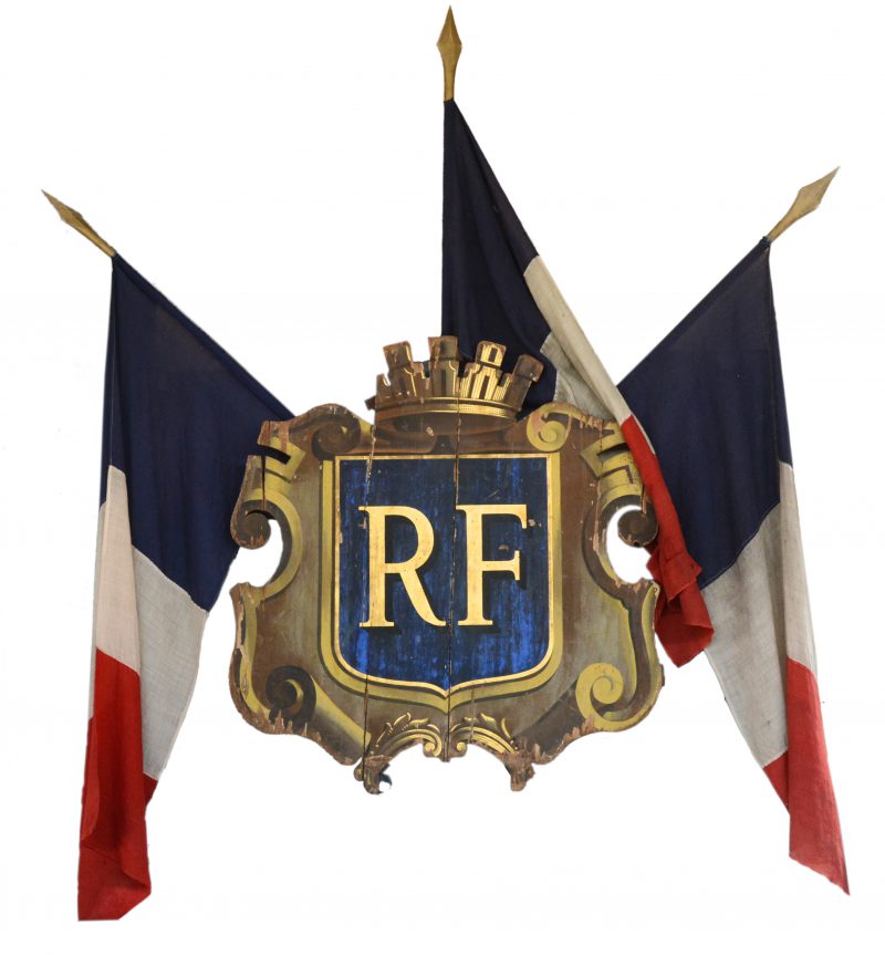 Een houten vlaggenstokhouder met houten voorplaat in de vorm van het wapenschild van de Franse Republiek. Met negen houders. We voegen er drie vlaggenstokken met Franse vlaggen aan toe.