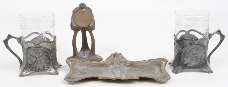 Vier art nouveau voorwerpen. Twee theeglazen met verzilverde houders en geslepen glas, gemerkt WMF, een horlogehoudertje van brons, een schaaltje met personage.