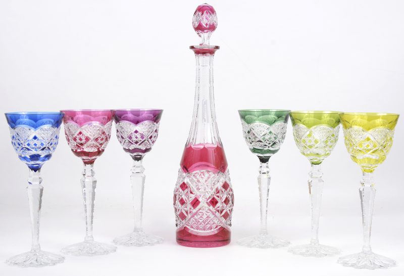 Een karaf en zes glazen van geslepen kristal in verschillende kleuren.