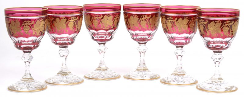 Een reeks van zes rodewijnglazen van geslepen kristal, versierd met een gegraveerd en verguld decor van wijnranken op een rode kelk en met kleurloze voet. Onderaan gemerkt.