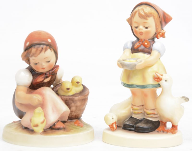 “Meisje met ganzen” & “Meisje met kuikentjes”. Twee beeldjes van meerkleurig porselein naar ontwerp van M. I. Hummel. Gemerkt.