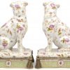 Een paar zittende hondjes op kussens. Meerkleurig aardewerk, versierd met een bloemendecor en met bronzen ornamenten. Onderaan gemerkt.