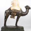 “Vrouw met kruik op kameel”. Een beeld van gepatineerd brons en gesculpteerd albast. Manco’s en restauraties aan het albast. De groen marmeren sokkel gebroken.