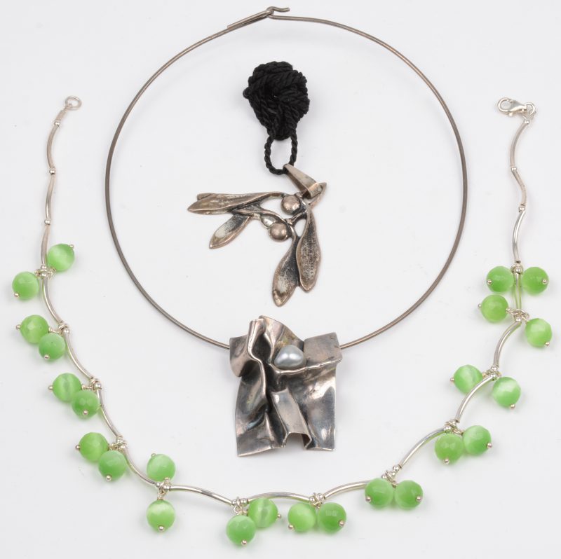 Drie verschillende halssnoeren van zilver waarvan één bezet met een grijze parel gemerkt achteraan en één bezet met kralen van groene agaat.