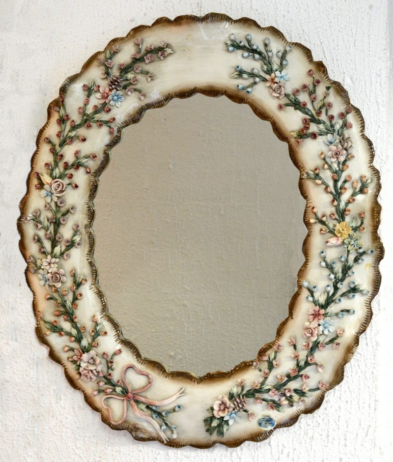 Een spiegel in porseleinen lijst, versierd met meerkleurige bloemen in reliëf.