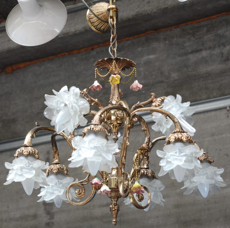 Een messingen luchter met negen lichtpunten met bloemvormige kapjes van gesatineerd glas en versierd met porseleinen bloempjes.