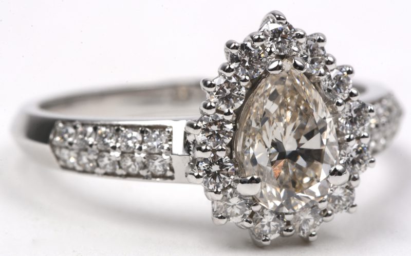 Een 18 karaats wit gouden ring bezet met een centrale druppelvormige diamant van ± 1,01 ct. H. VSI. en briljanten met een gezamenlijk gewicht van ± 0,53 ct.