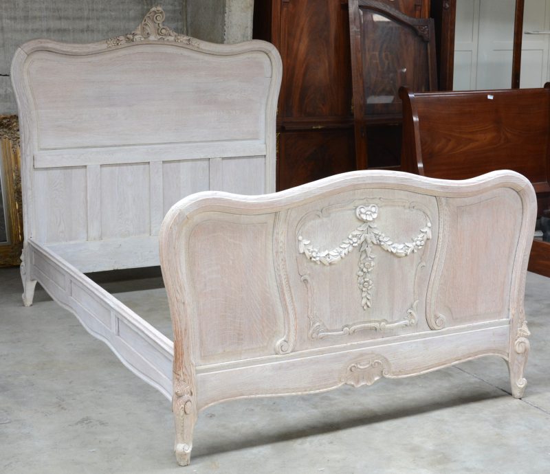 Een grijsgepatineerd houten bedframe met gesculpteerde kuif in Lodewijk XV-inspiratie en bloemenstrikken.
