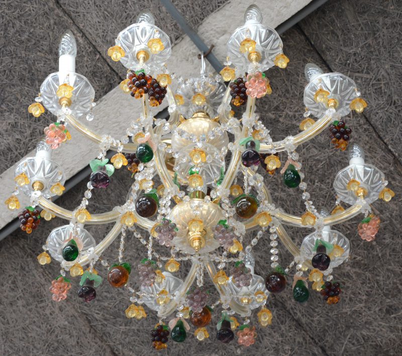 Een grote Maria-Theresialuchter met tien lichtarmen, versierd met meerkleurige glazen bloempjes, peertjes en druiventrossen.