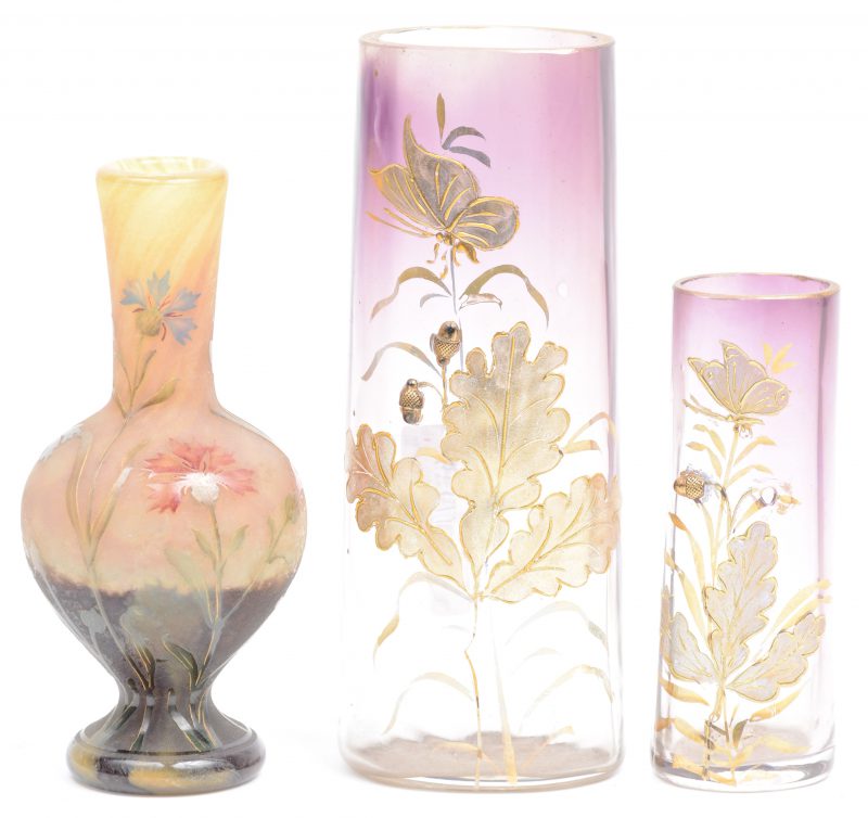 Drie glazen vaasjes, waarbij twee met een handgeschilderd verguld bladerdecor en een klein vaasje met geëtst bloemendecor. Het laatste gemerkt Daum, Nancy.