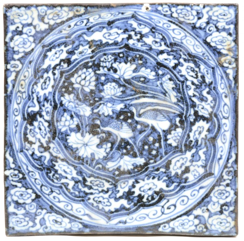 Een tegel van Chinees porselein met een blauw op wit decor van vogels en bloemen.