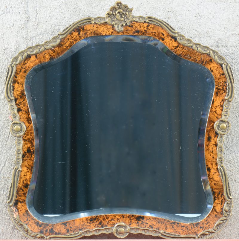 Een spiegel in Lodewijk XV-stijl met lijst van messing en hout in wortelnootimitatie.