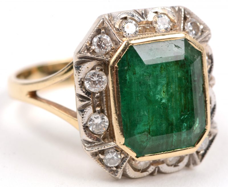 Een 14 karaats wit en geel gouden ring bezet met diamanten met een gezamenlijk gewicht van +- 0,30 ct. en een smaragd van +- 5 ct.