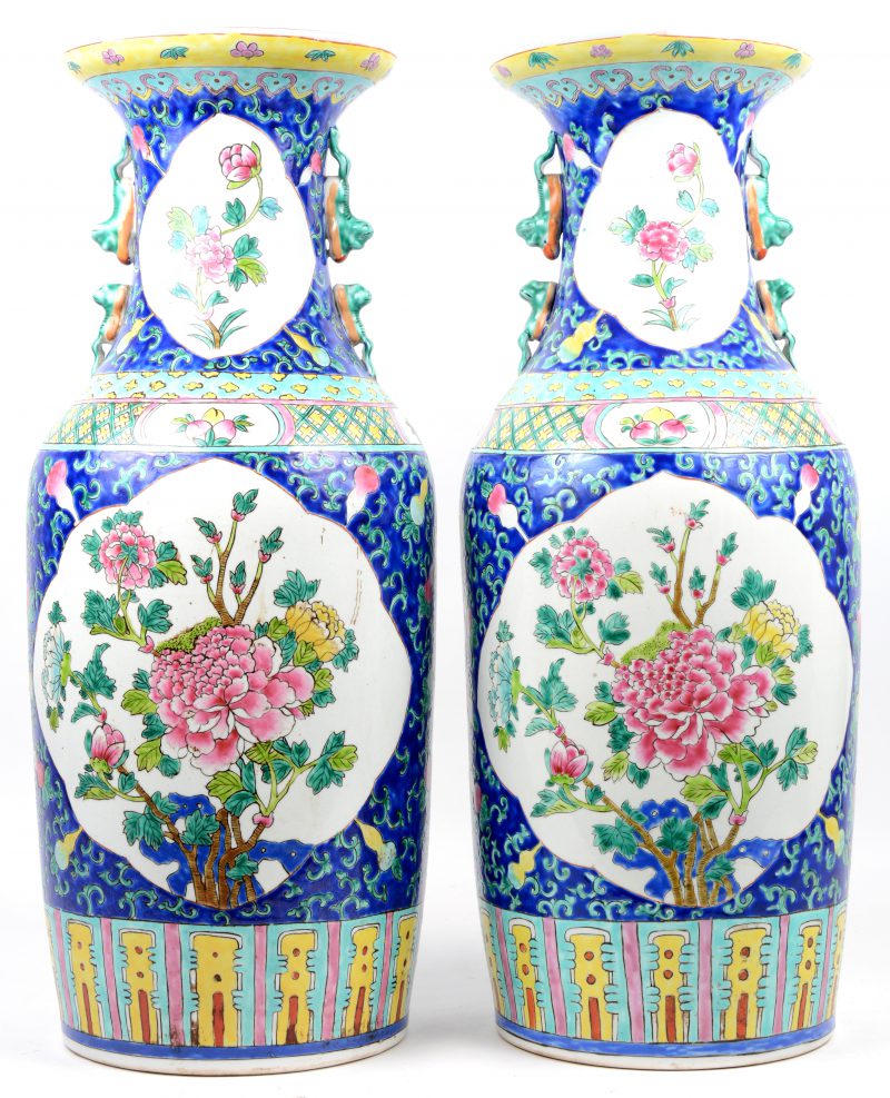 Een paar vazen van Chinees porselein met een decor van pioenen in cartouches met erond een vruchten op een blauwe achtergrond. Onderaan gemerkt.
