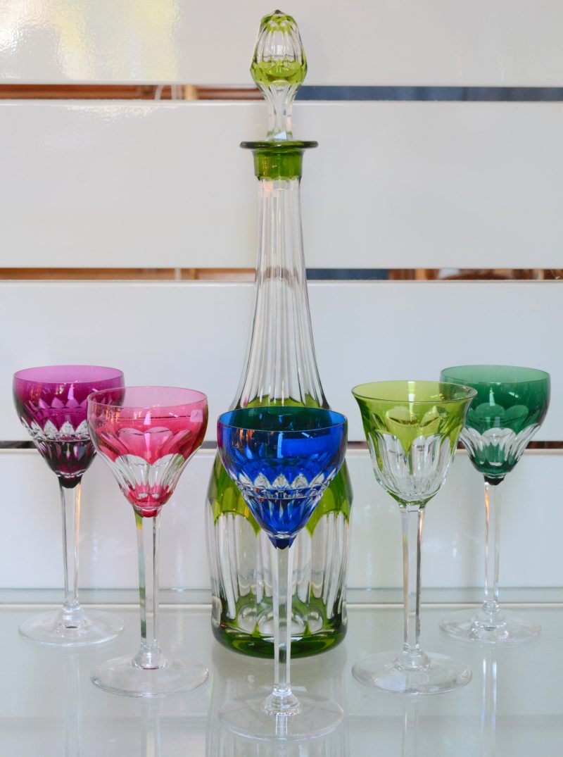Een karaf en vijf glazen (3 verschillende modellen) van geslepen kristal in verschillende kleuren.