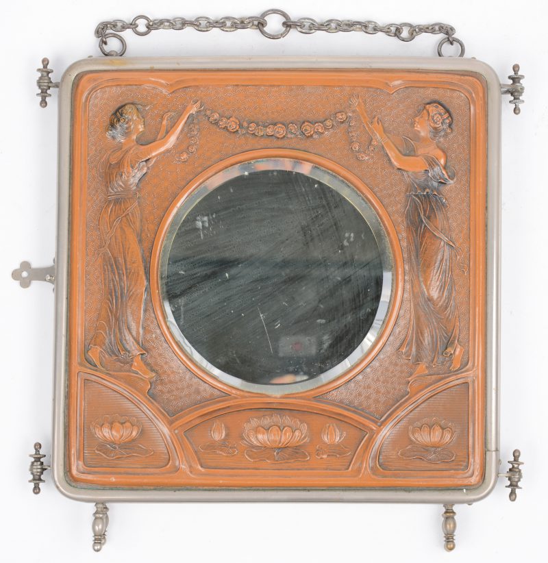 Een reisspiegel van metaal met een mooie voorplaat van gedreven bruin leder en drie spiegelpanelen en een ketting. Twee ruitjes gebarsten. Omstreeks 1900.