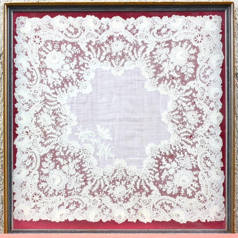 Een vierkante zakdoekje met een brede boord van rosalinekant. Ingelijst.