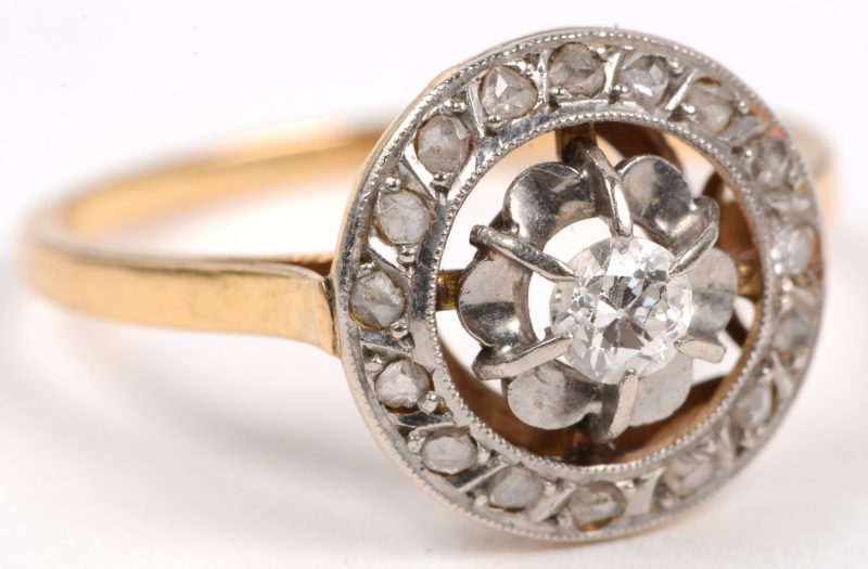 Een 18 karaats wit en geel gouden ring bezet met diamanten oude slijp met een gezamenlijk gewicht van +- 0,16 ct. en een centrale briljant van +- 0,10 ct.