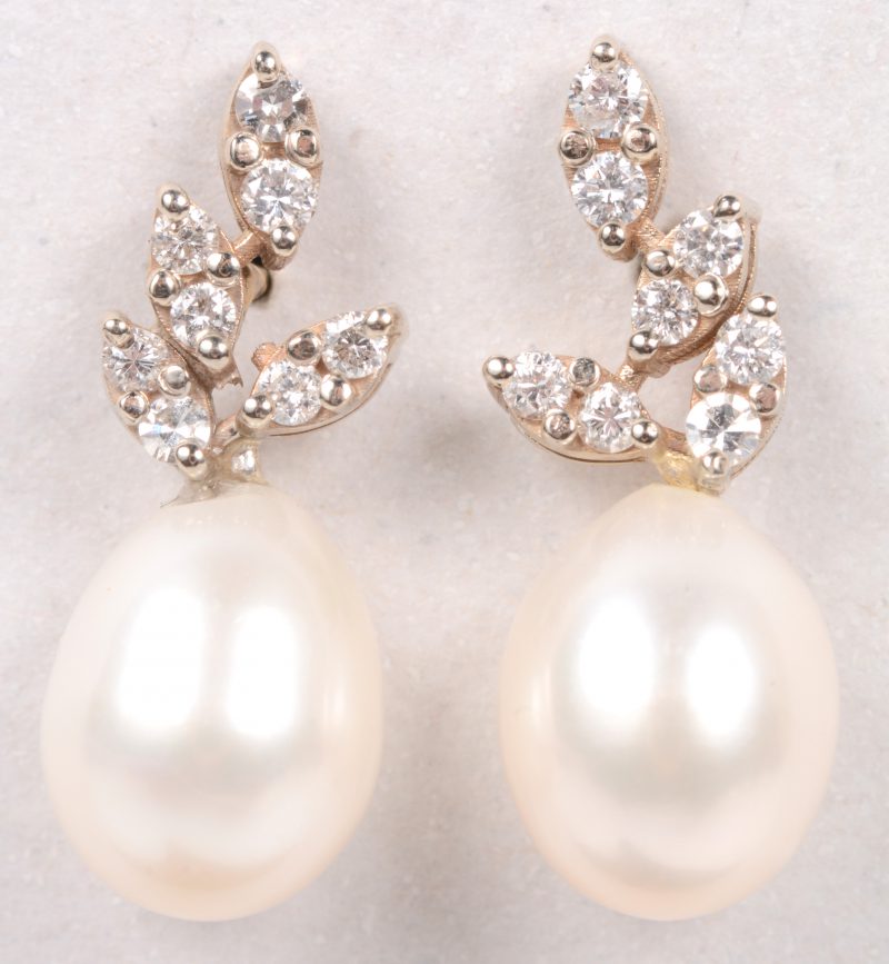 Een paar 18 karaats wit gouden oorbellen bezet met briljanten met een gezamenlijk gewicht van +- 0,20 ct. en twee parels.
