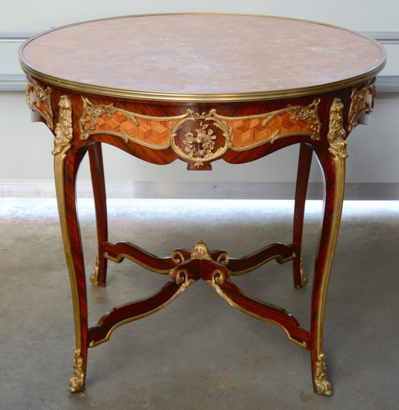 Een gefineerde ronde tafel in Lodewijk XV-stijl, versierd met verguld beslag en met marmeren blad.
