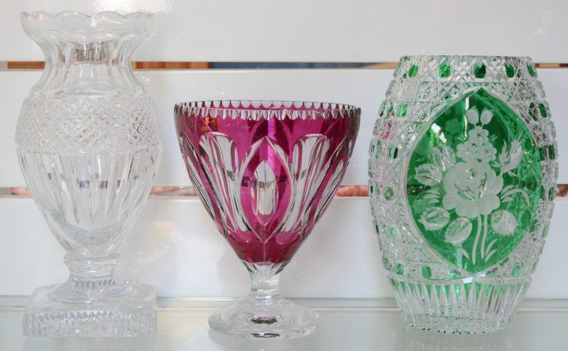 Een lot geslepen kristal, bestaande uit een kleurloze vaas, een vaas met bloemendecor op groene achtergrond en een mauve gedubbelde coupe op voet. De laatste met randschilfer.